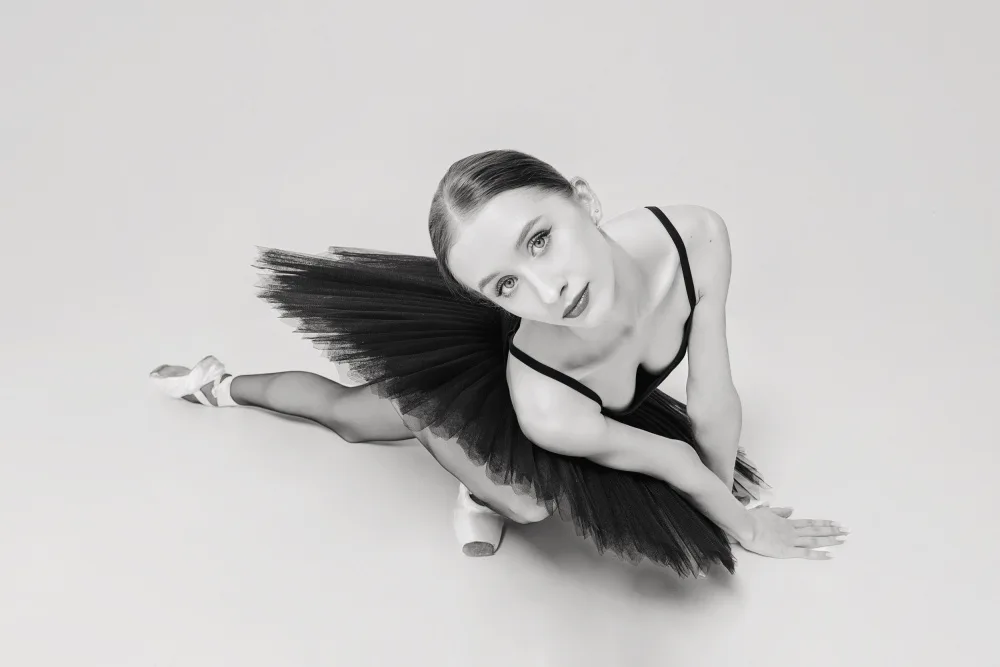 Alexandr: portrait of a ballerina in a black tutu lying on the floor leaning on her hands top view