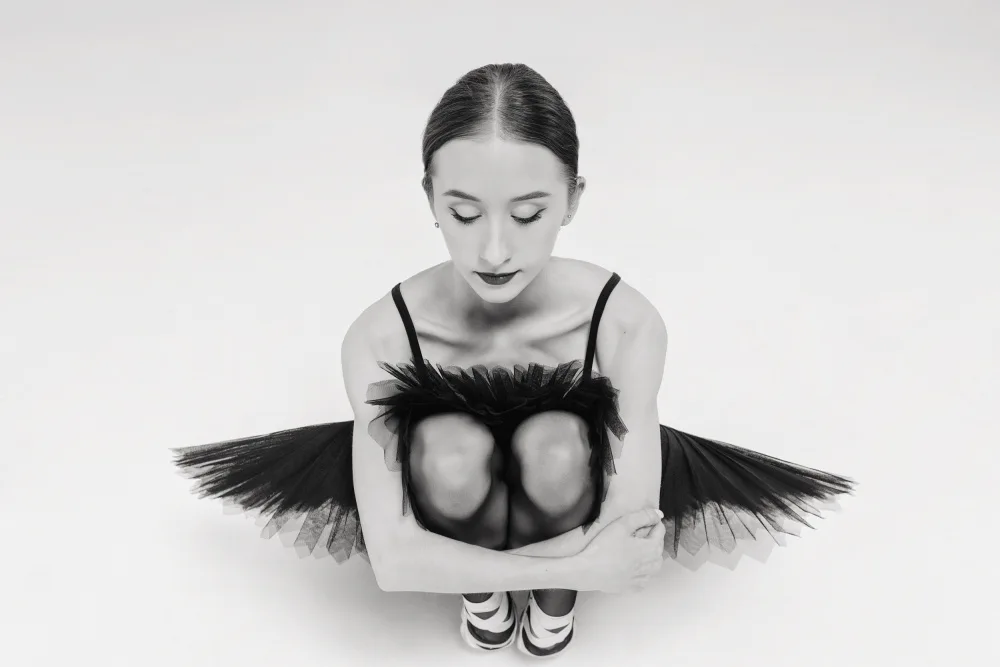 Alexandr: a portrait of a ballerina in a black tutu squatting hugging her knees