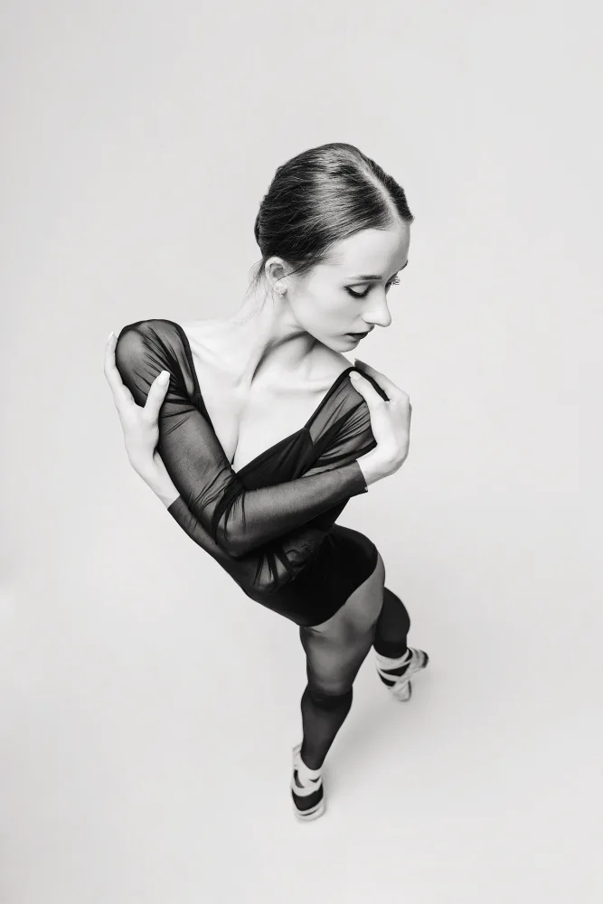 Alexandr: portrait of a ballerina in a black bodysuit top view standing with her arms around her shoulders