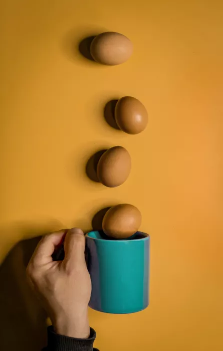 Enrique: Eier in einer Reihe auf orangefarbenem Hintergrund mit einer Hand, die eine türkisfarbene Tasse hält