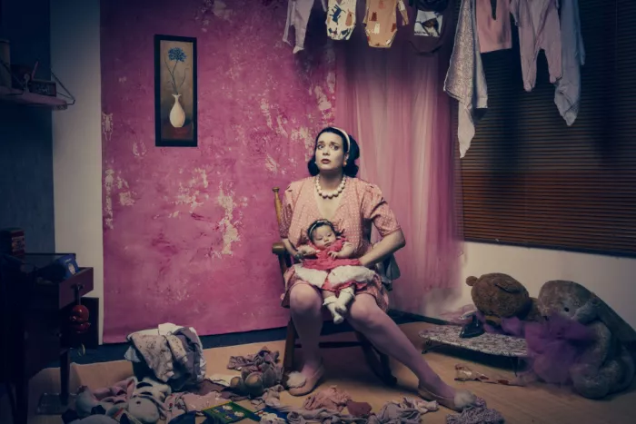 Mighorst, Ineke: Mother holding her baby while surrounded by scattered  laundry in a disheveled room.